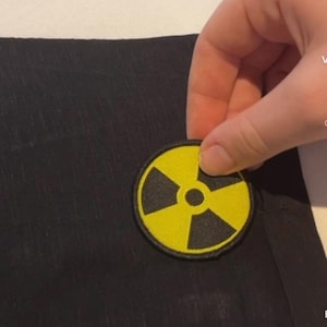 May include: A black fabric patch with a yellow radiation symbol. The symbol is a circle with a black centre and three black blades radiating out from the centre.