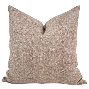 May include: A square decorative pillow with a floral pattern in shades of mauve and cream. The pillow features a repeating design of small flowers and leaves, creating a textured appearance. The pillow is made of a soft fabric.