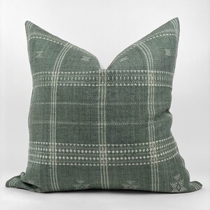 May include: A green and white patterned throw pillow with a woven texture. The pillow has a square shape and a subtle geometric design.