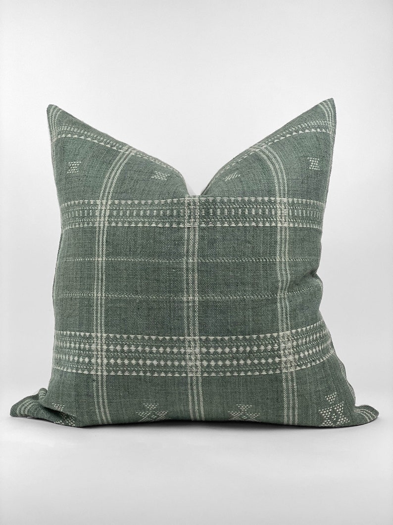 May include: A green and white patterned throw pillow with a woven texture. The pillow has a square shape and a subtle geometric design.