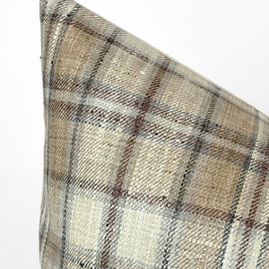 May include: Close-up of a beige and brown plaid pillow with a subtle woven texture.