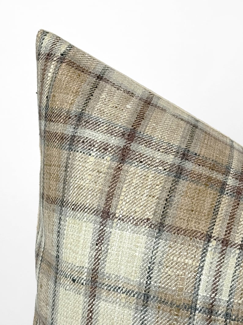 May include: Close-up of a beige and brown plaid pillow with a subtle woven texture.