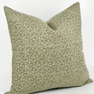 May include: A green pillow with a white floral pattern. The pillow is made of a soft, linen fabric.