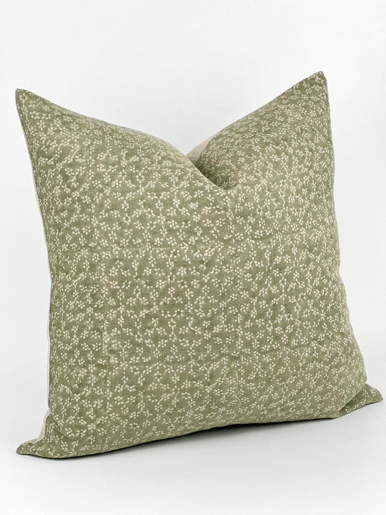 May include: A green pillow with a white floral pattern. The pillow is made of a soft, linen fabric.
