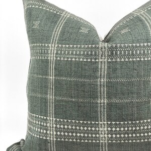 May include: A green and white patterned throw pillow with a woven texture. The pillow has a square shape and a subtle geometric design.