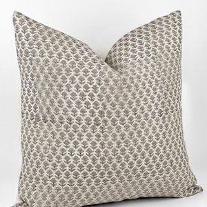 May include: A square throw pillow with a white background and a brown floral pattern. The pillow is made of a soft, textured fabric.