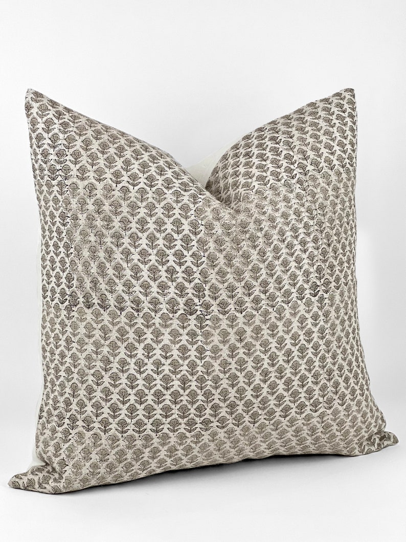 May include: A square throw pillow with a white background and a brown floral pattern. The pillow is made of a soft, textured fabric.