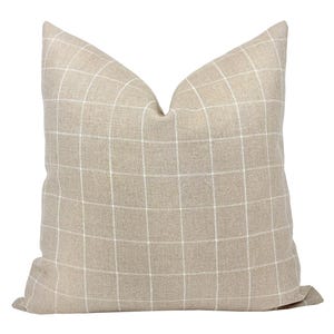 May include: A beige throw pillow with a white grid pattern. The pillow is made of a soft, textured fabric.