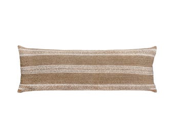 May include: A long, rectangular cushion featuring horizontal stripes in shades of brown and cream. The cushion has a textured appearance, suggesting a woven fabric. Suitable for a bed or sofa, this is a decorative item.