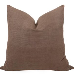 May include: A square, brown cushion with a textured fabric. The cushion is a solid colour and has a soft, inviting appearance. The cushion is designed for home decor and adds a touch of warmth to any room.