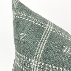 May include: A green and white patterned throw pillow with a woven texture. The pillow is made of a soft, comfortable fabric and has a subtle geometric design.