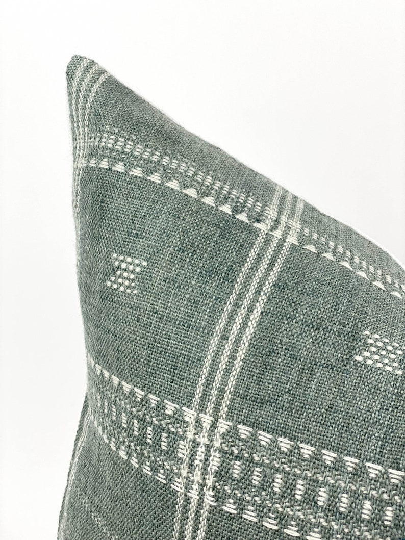May include: A green and white patterned throw pillow with a woven texture. The pillow is made of a soft, comfortable fabric and has a subtle geometric design.