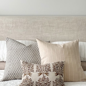 May include: A bed with a linen headboard and three pillows. The pillows are a patterned gray and white, a striped beige, and a brown floral print.