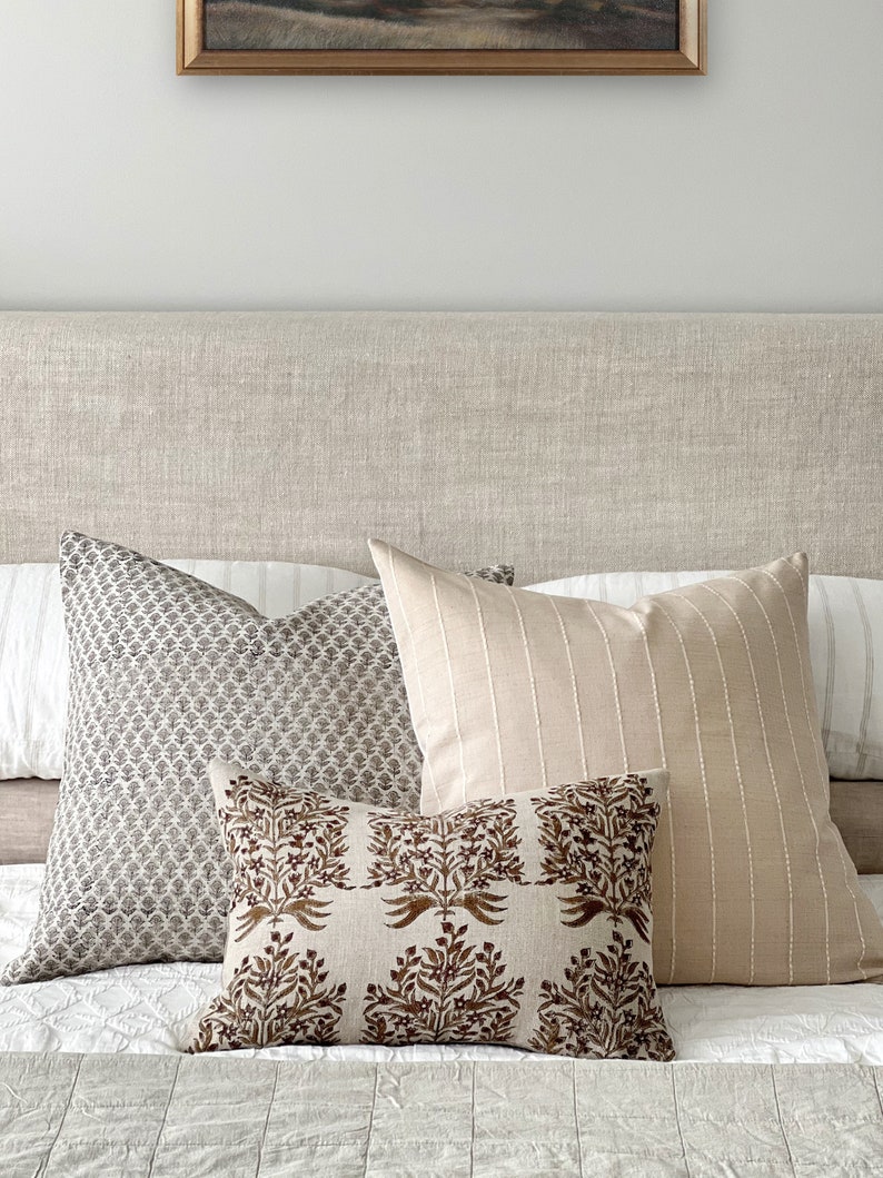 May include: A bed with a linen headboard and three pillows. The pillows are a patterned gray and white, a striped beige, and a brown floral print.