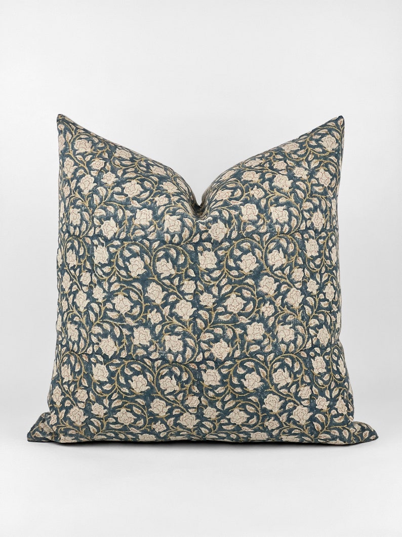 May include: A teal blue throw pillow with a white floral pattern. The pillow has a square shape and is made of a soft fabric.