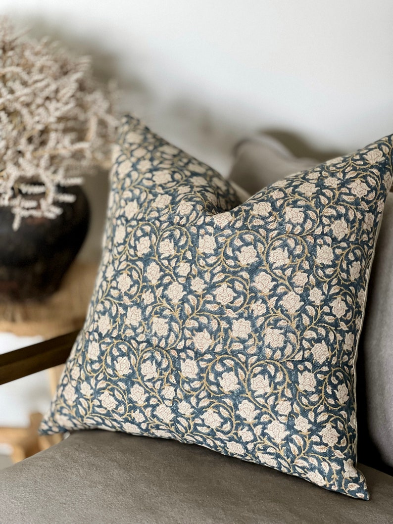 May include: A blue and white floral patterned throw pillow with a subtle gold accent. The pillow is made of a soft, textured fabric and is perfect for adding a touch of elegance to any room.