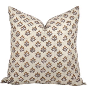May include: A beige cushion with a repeating pattern of small brown and purple floral designs.