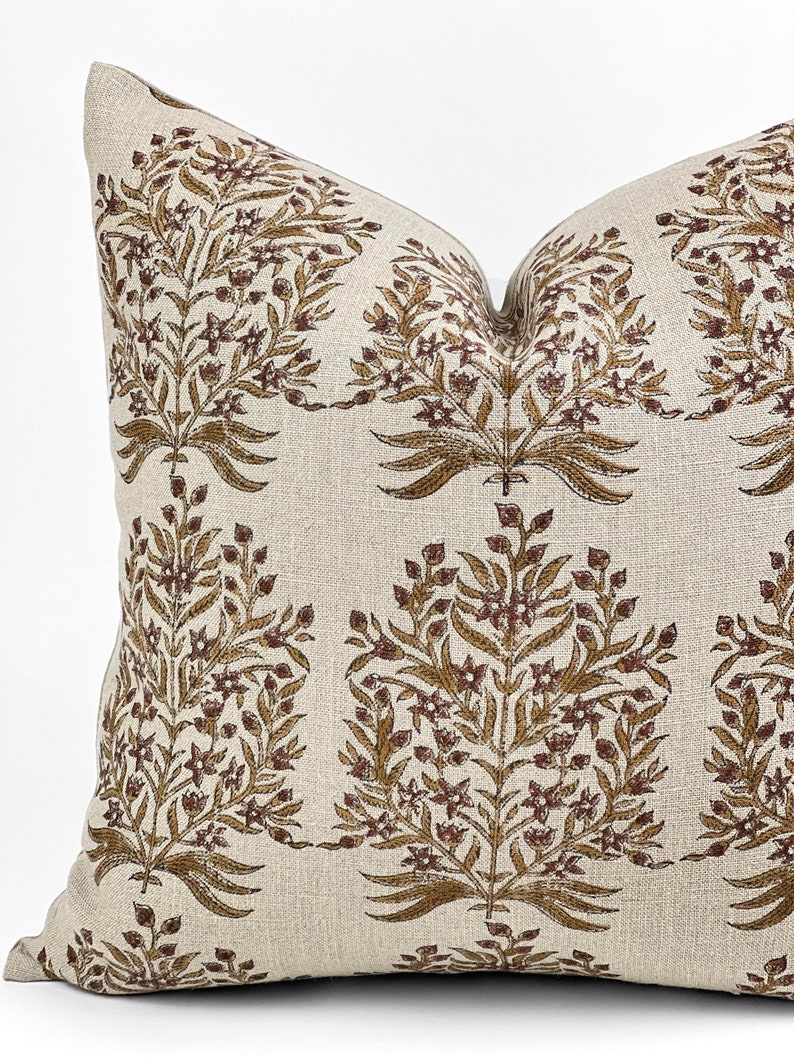 May include: A beige linen pillow with a brown floral pattern. The pillow has a square shape and a subtle texture.