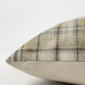 May include: A brown and beige plaid pillow with a zipper closure. The pillow is made of a soft, woven fabric.