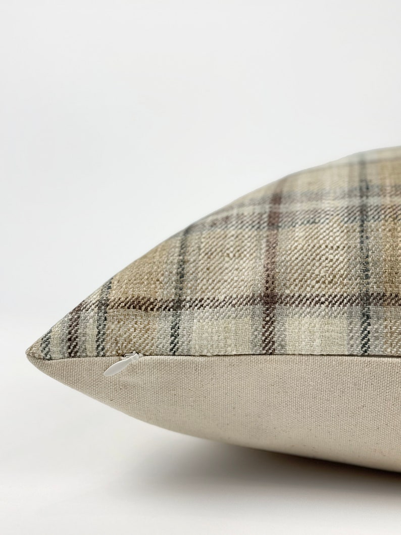 May include: A brown and beige plaid pillow with a zipper closure. The pillow is made of a soft, woven fabric.