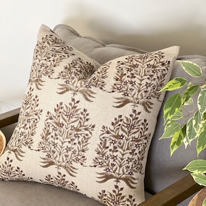 May include: A beige throw pillow with a brown floral pattern. The pillow is sitting on a brown couch.
