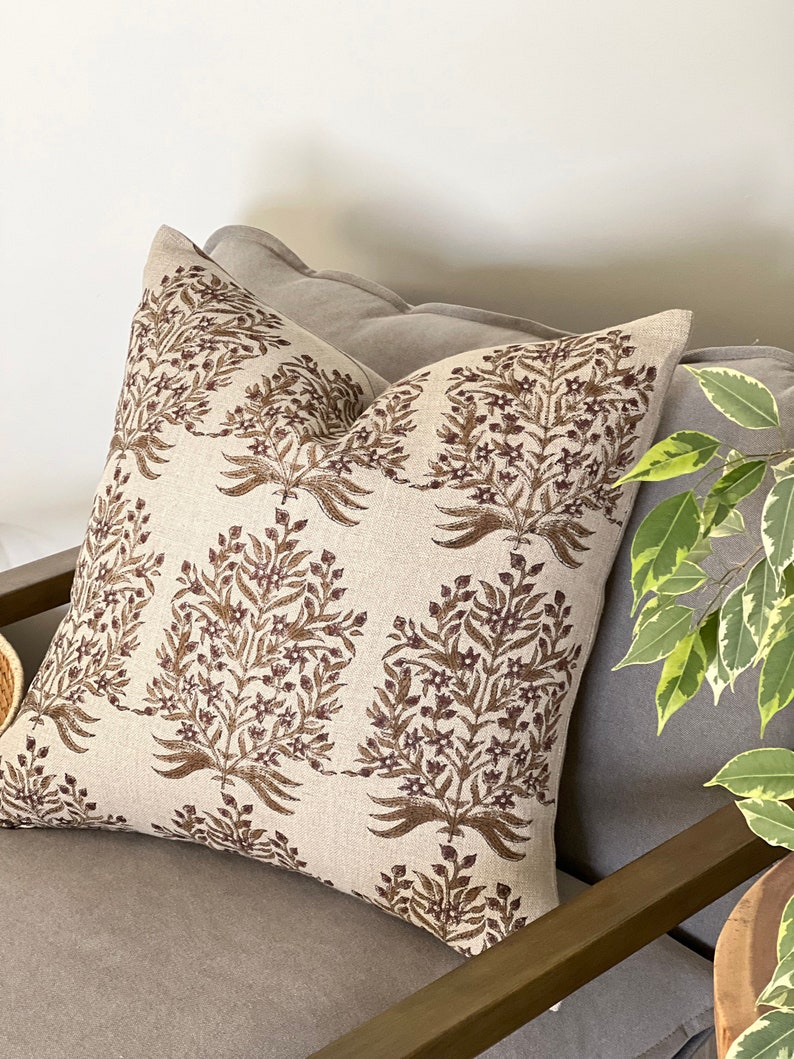 May include: A beige throw pillow with a brown floral pattern. The pillow is sitting on a brown couch.