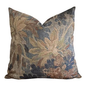 May include: Decorative throw pillow with a floral pattern in shades of brown, blue, and beige. The pillow has a textured appearance and a square shape, suitable for a sofa or bed.