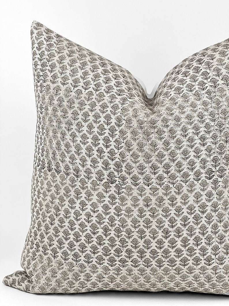 May include: A square throw pillow with a white background and a repeating pattern of small black floral designs.
