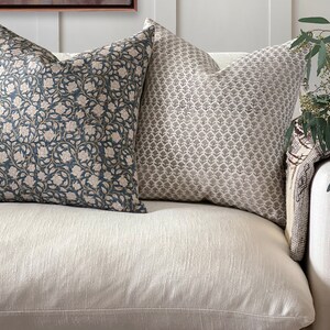 May include: Two decorative throw pillows on a white couch. The pillow on the left has a blue background with a floral pattern in shades of brown and white. The pillow on the right has a gray background with a geometric pattern in shades of gray.
