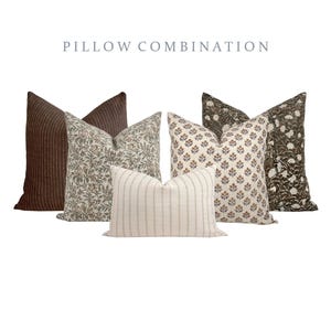 May include: A selection of decorative cushions in different patterns and colours. The cushions feature a brown ribbed design, floral prints in neutral tones, and a striped cushion. The text "PILLOW COMBINATION" is displayed at the top.