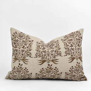 May include: A beige linen pillow with a brown floral pattern. The pillow has a rectangular shape and is decorated with a repeating design of stylized flowers and leaves.