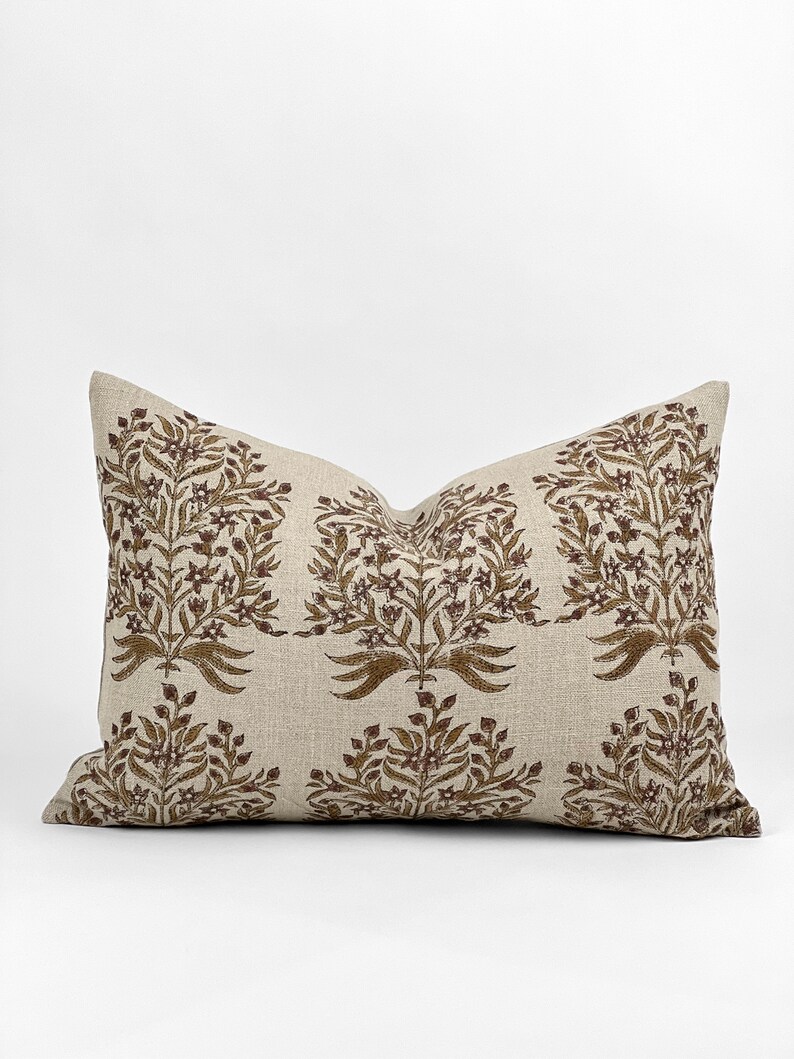 May include: A beige linen pillow with a brown floral pattern. The pillow has a rectangular shape and is decorated with a repeating design of stylized flowers and leaves.