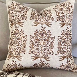May include: A beige throw pillow with a brown floral pattern. The pillow is made of linen and has a subtle texture.