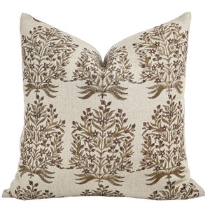 May include: A beige linen pillow with a brown floral pattern. The pattern features stylized branches with small flowers and leaves.