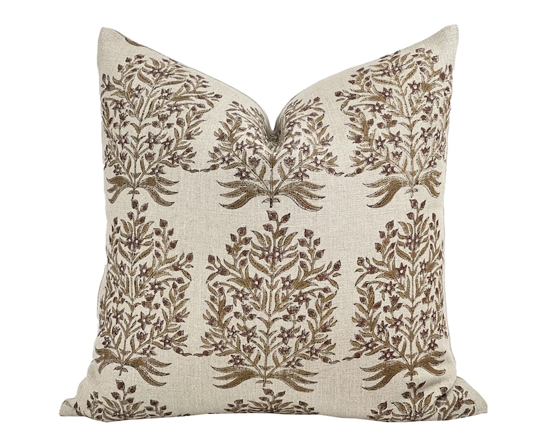 May include: A beige linen pillow with a brown floral pattern. The pattern features stylized branches with small flowers and leaves.