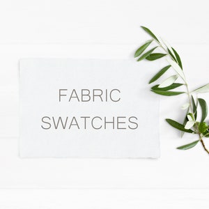 May include: A white card with the text "FABRIC SWATCHES" on a white wooden background with a green olive branch.