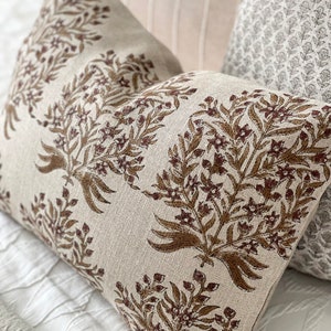 May include: A beige pillow with a brown floral pattern. The pillow is made of a soft, textured fabric and has a subtle sheen.