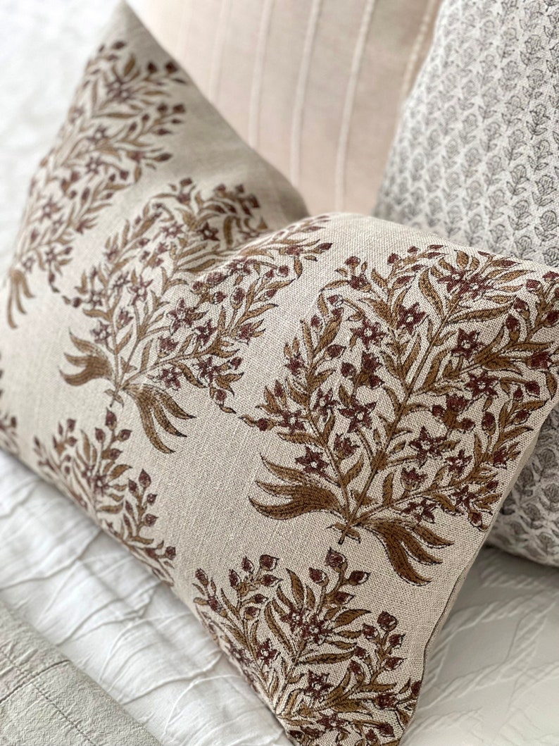 May include: A beige pillow with a brown floral pattern. The pillow is made of a soft, textured fabric and has a subtle sheen.