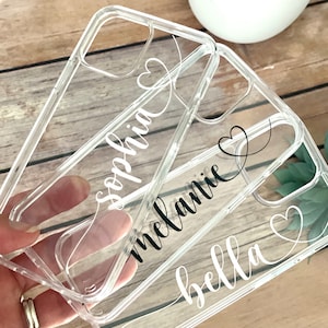 May include: Three clear phone cases with names and hearts printed on them. The names are Sophia, Melanie, and Bella.