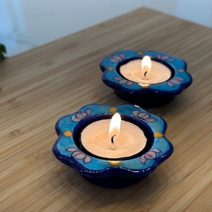 May include: Two blue and white ceramic tea light holders with floral designs. Each holder has a white tea light candle burning inside.