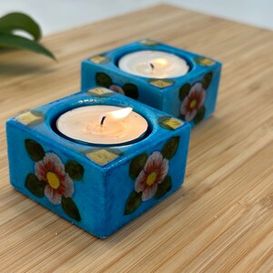 May include: Two teal blue ceramic candle holders with floral designs. Each holder has a small white tea light candle inside.