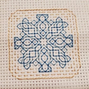 Könnte beinhalten: Quadratisches Kreuzstichmuster mit einem blauen geometrischen Schneeflockenmuster. Das Design ist von einem goldenen Rand umgeben und auf weißem Stoff gestickt. Die komplizierten Details des Kreuzstichs sind deutlich sichtbar.