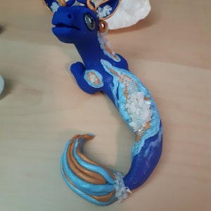 May include: A blue and gold dragon figurine with a crystal-like texture. The dragon has a long tail and a small head with large eyes. The figurine is made of polymer clay and is hand-painted.