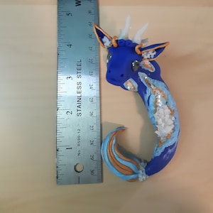 May include: A blue and gold dragon figurine with white horns and a glittery finish. The dragon is approximately 4 inches long and is made of polymer clay.