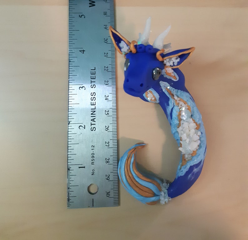 May include: A blue and gold dragon figurine with white horns and a glittery finish. The dragon is approximately 4 inches long and is made of polymer clay.