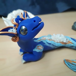 May include: A blue and gold dragon figurine with white crystals embedded in its back. The dragon has a long tail and a small, curled horn on its head.