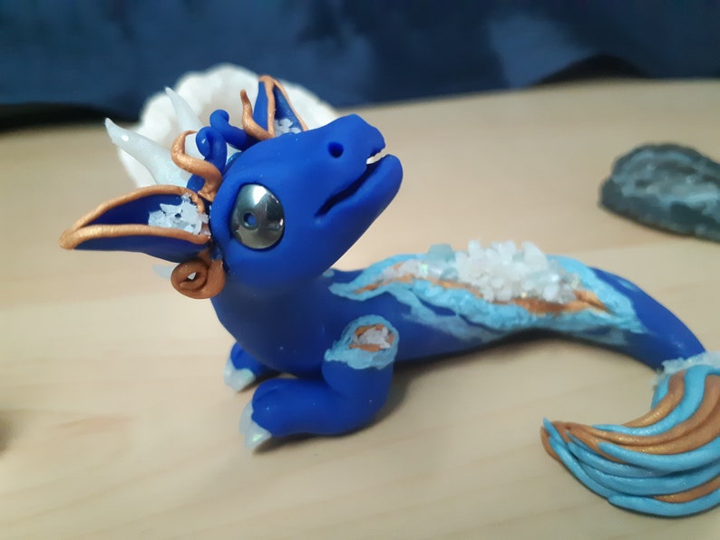 May include: A blue and gold dragon figurine with white crystals embedded in its back. The dragon has a long tail and a small, curled horn on its head.