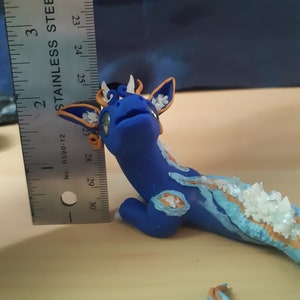May include: A blue and gold dragon figurine with white crystals on its back. The dragon is about 3 inches long and is made of polymer clay.