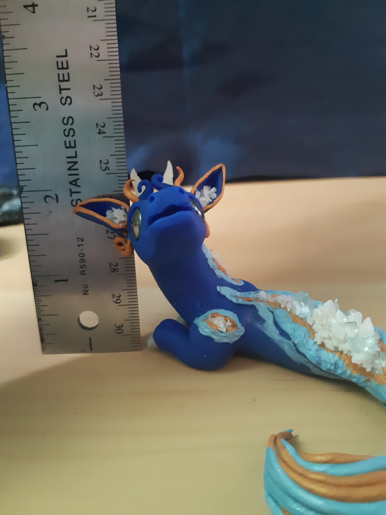 May include: A blue and gold dragon figurine with white crystals on its back. The dragon is about 3 inches long and is made of polymer clay.