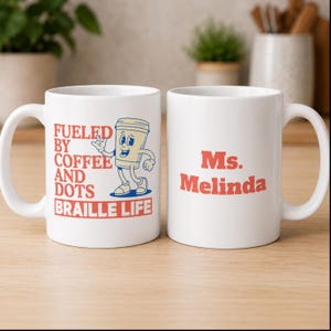 May include: Two white ceramic mugs featuring red and blue text and graphics. One mug displays a cartoon coffee cup character with the text FUELED BY COFFEE AND DOTS BRAILLE LIFE. The other mug features the red text Ms. Melinda on the front surface.